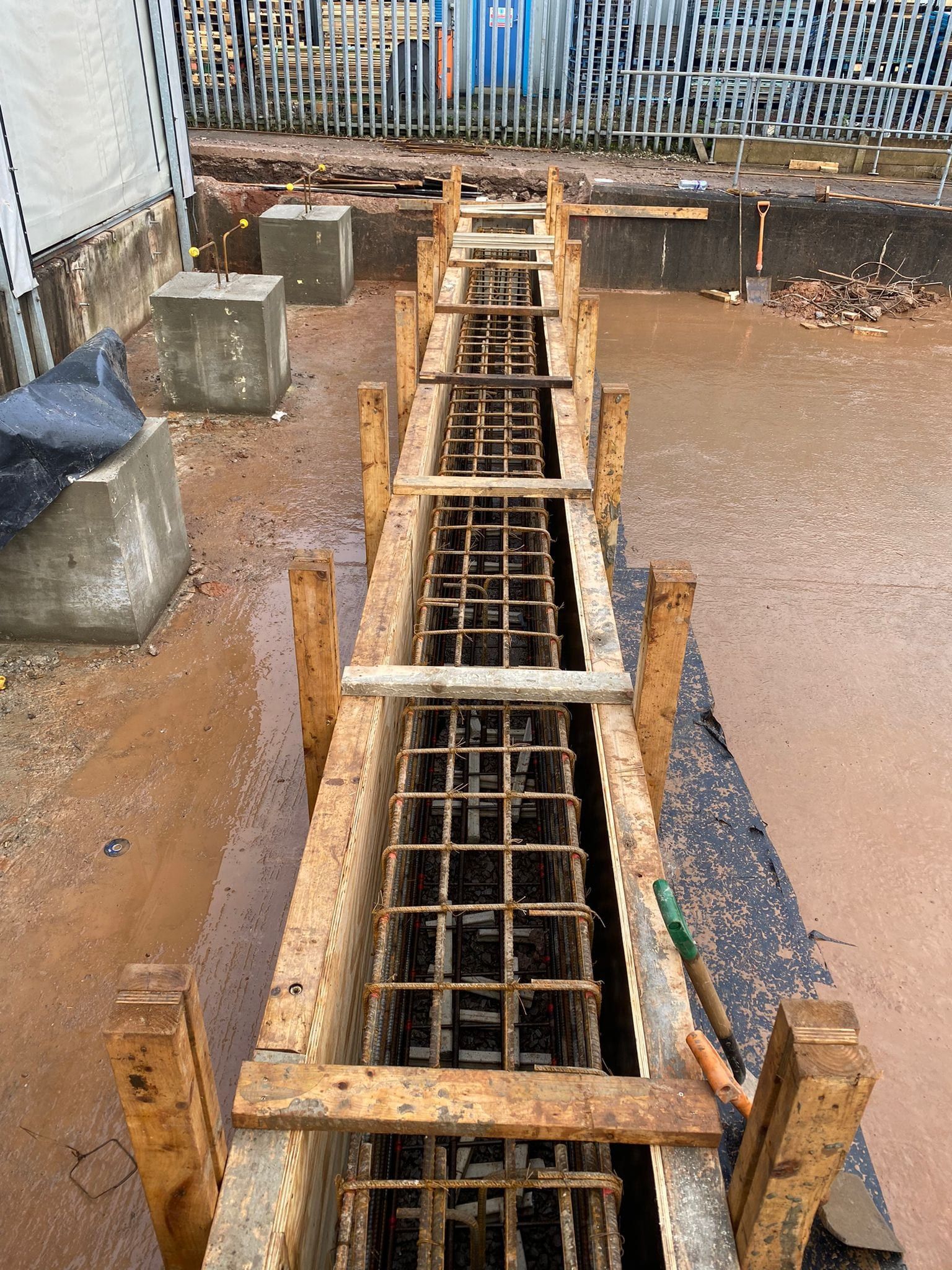 Timber shuttering and soldiers holding a ground beam reinforcement cage before the pour