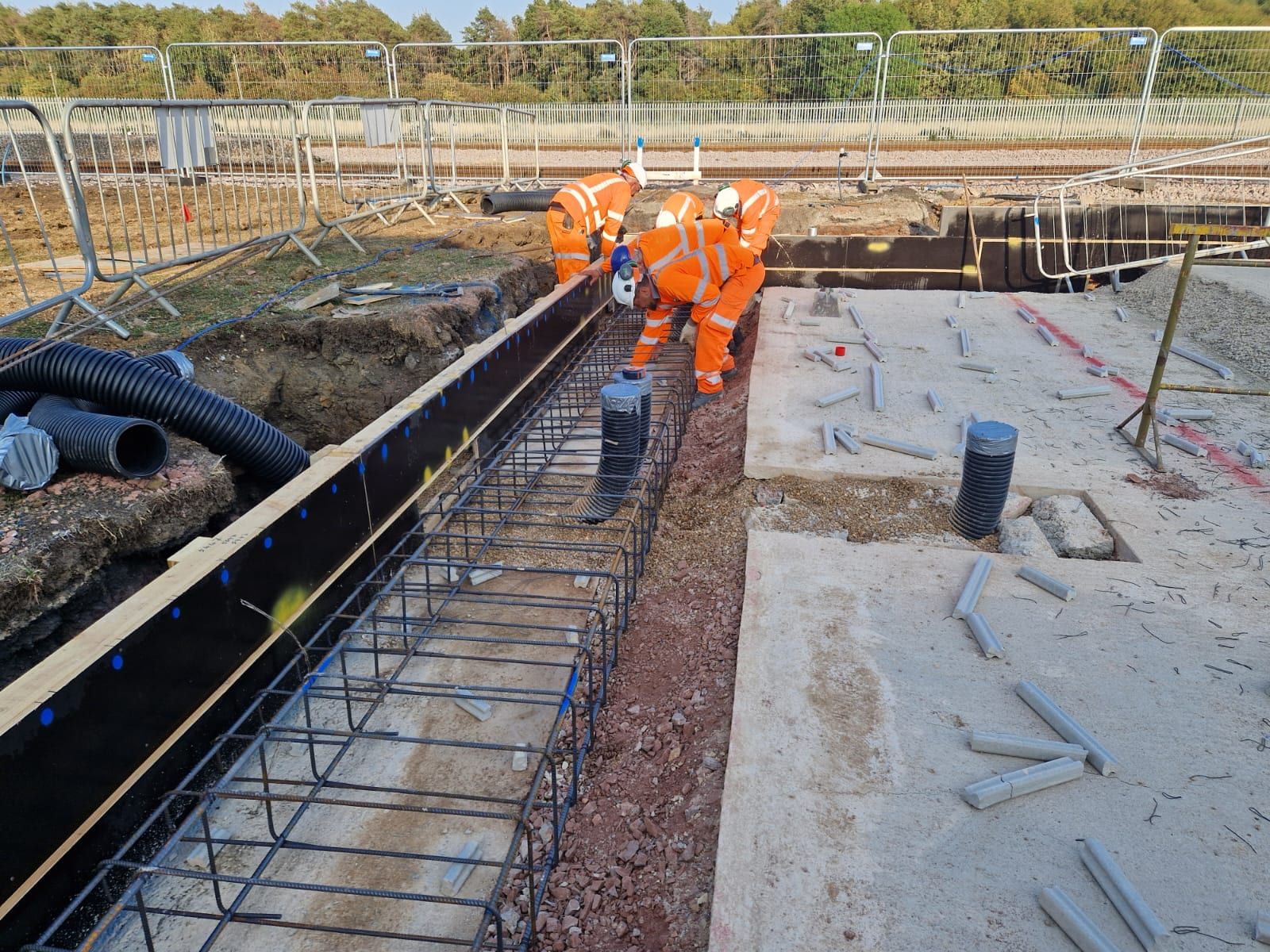 Groundworkers lowering a ground beam reinforcement cage into timber shuttering