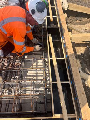 Steel fixer tying reinforcement bars with pliers over a ground beam cage
