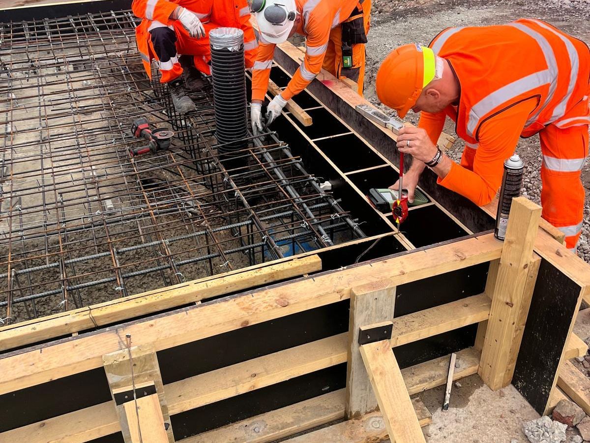 Three workers checking the level of a timber shutter beside a steel reinforcement mat